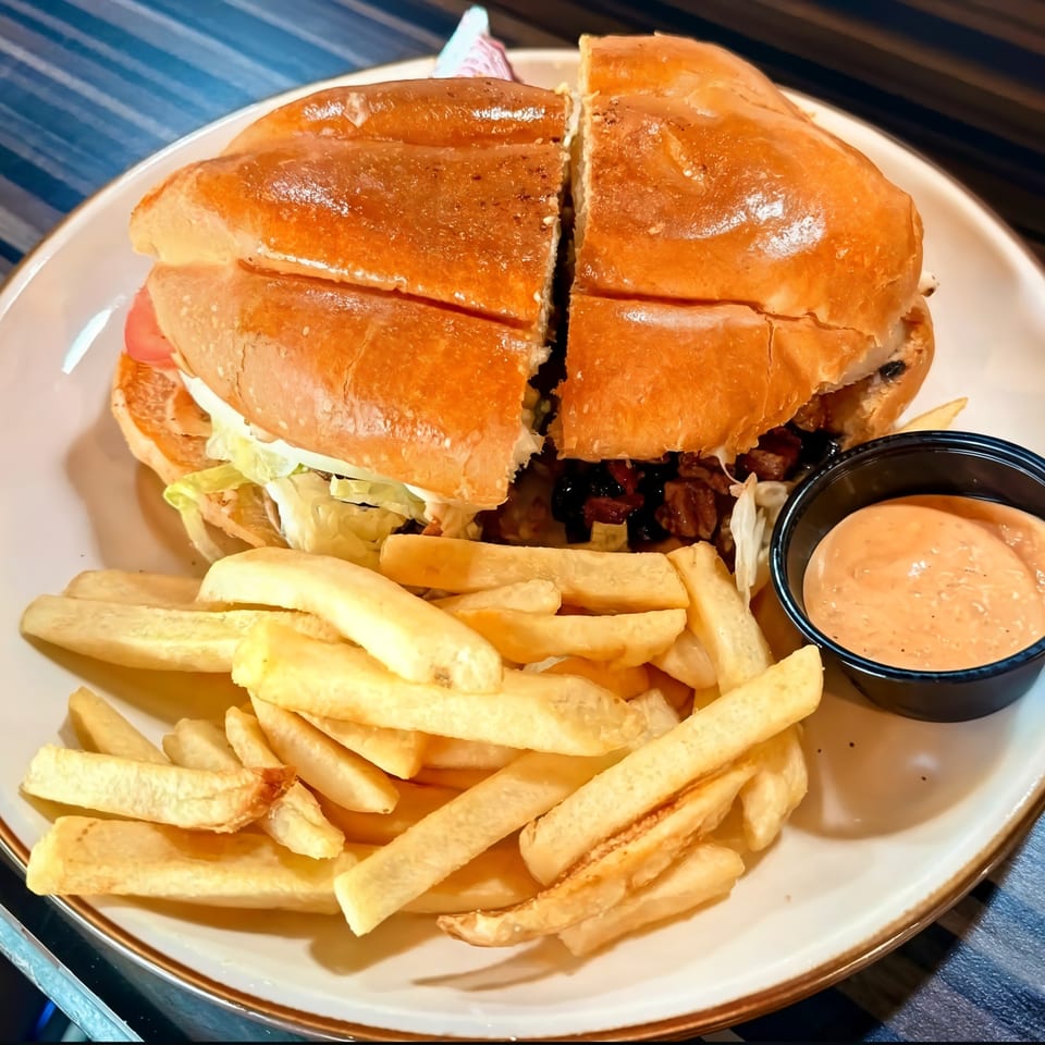 A Mexican torta sandwich, cut in half, with fries and a side of dipping sauce on a white plate.