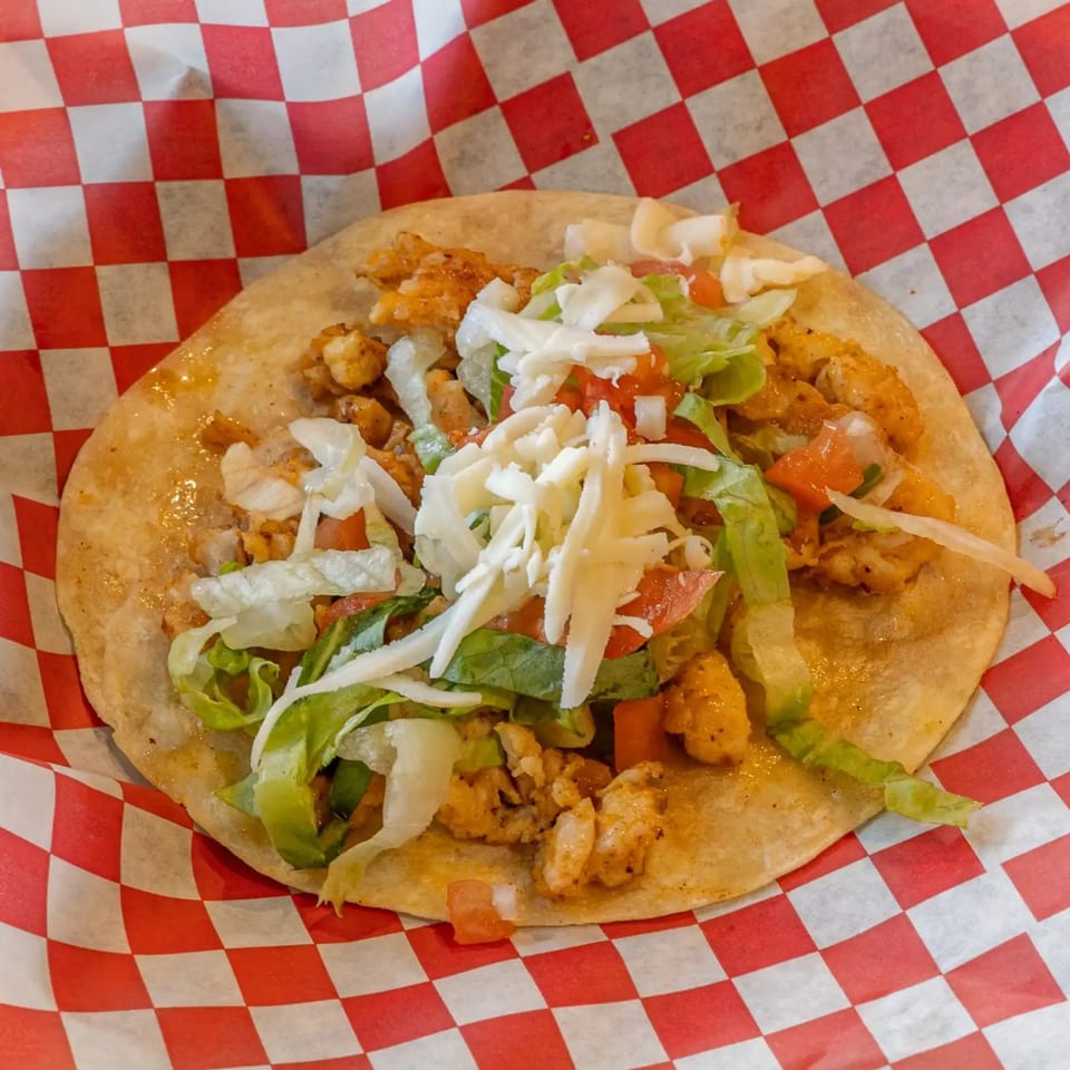 A chicken taco from El Rey Tacos & Beer, topped with lettuce, pico de gallo, and shredded cheese.