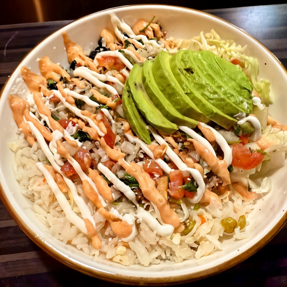 A vibrant Mexican rice bowl with sliced avocado, pico de gallo, and creamy sauces.